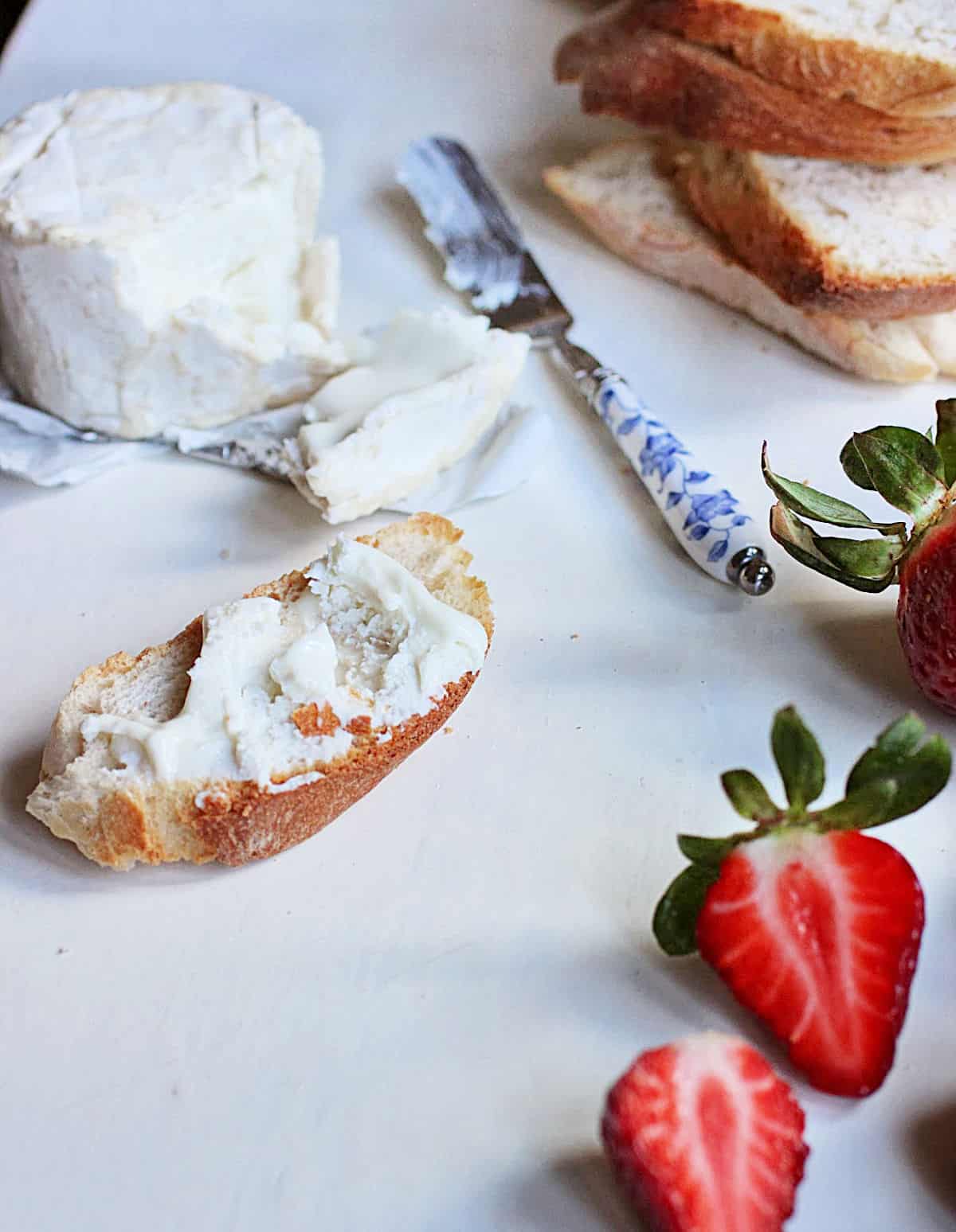 White table with cheese, knife, bread slices, fresh strawberries