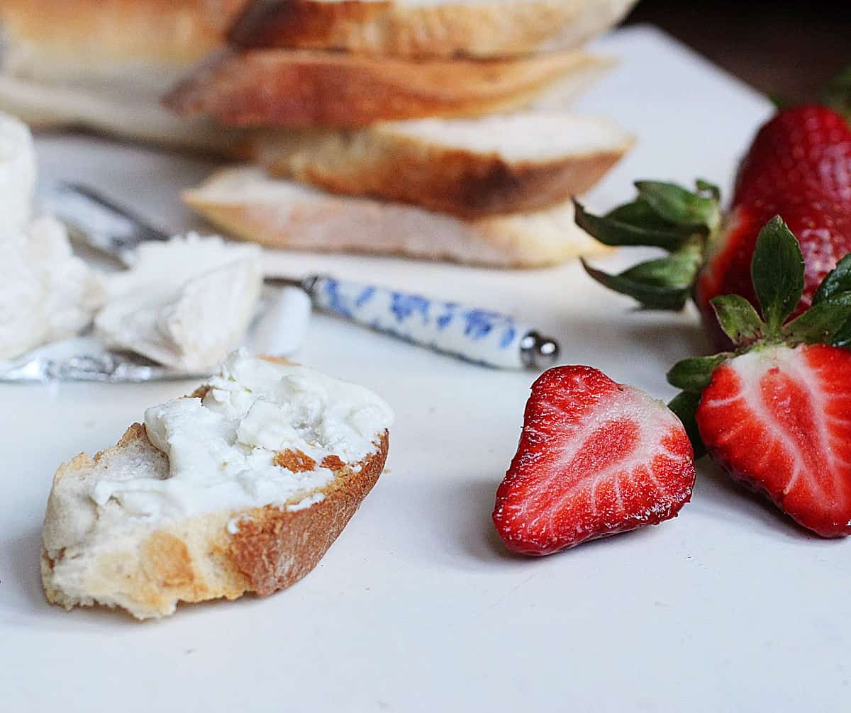 Slicce of bread with cheese, stack of bread slices, cut fresh strawberries, all on white surface