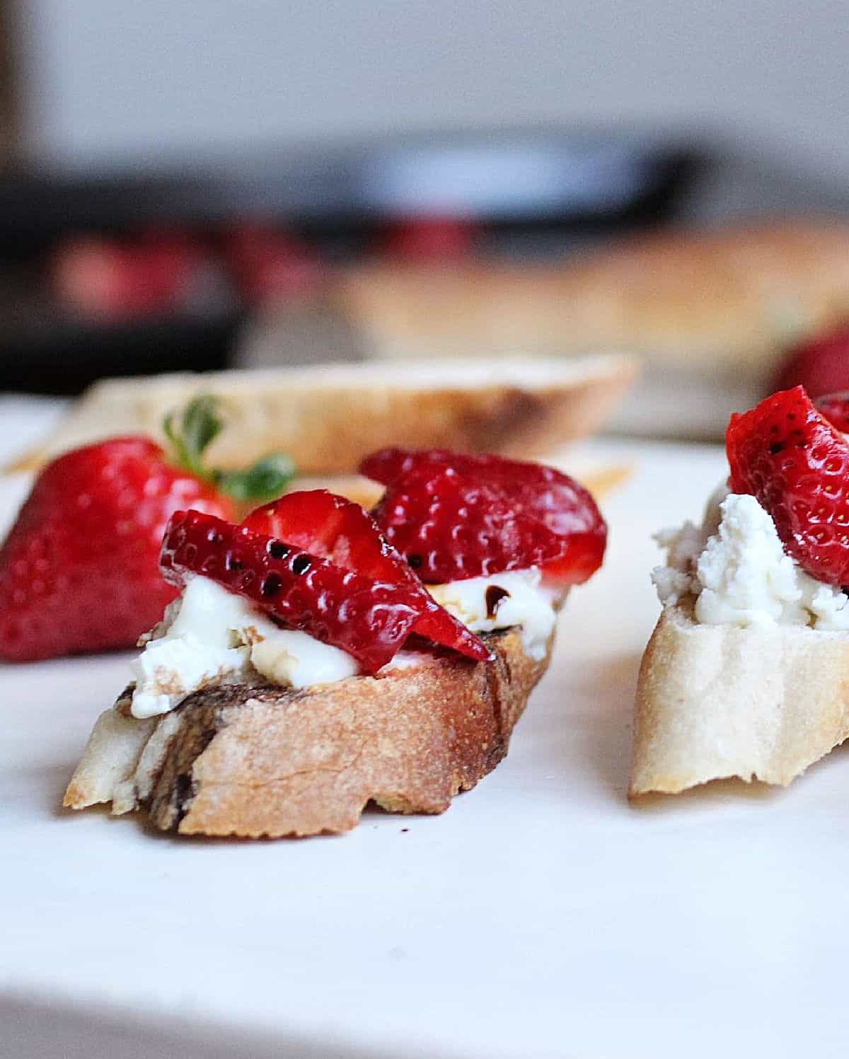 Slices of bread with cheese and strawberries on white table