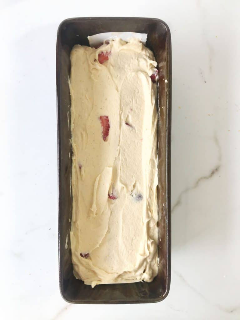 Loaf pan on a white marble surface with strawberry pound cake batter.