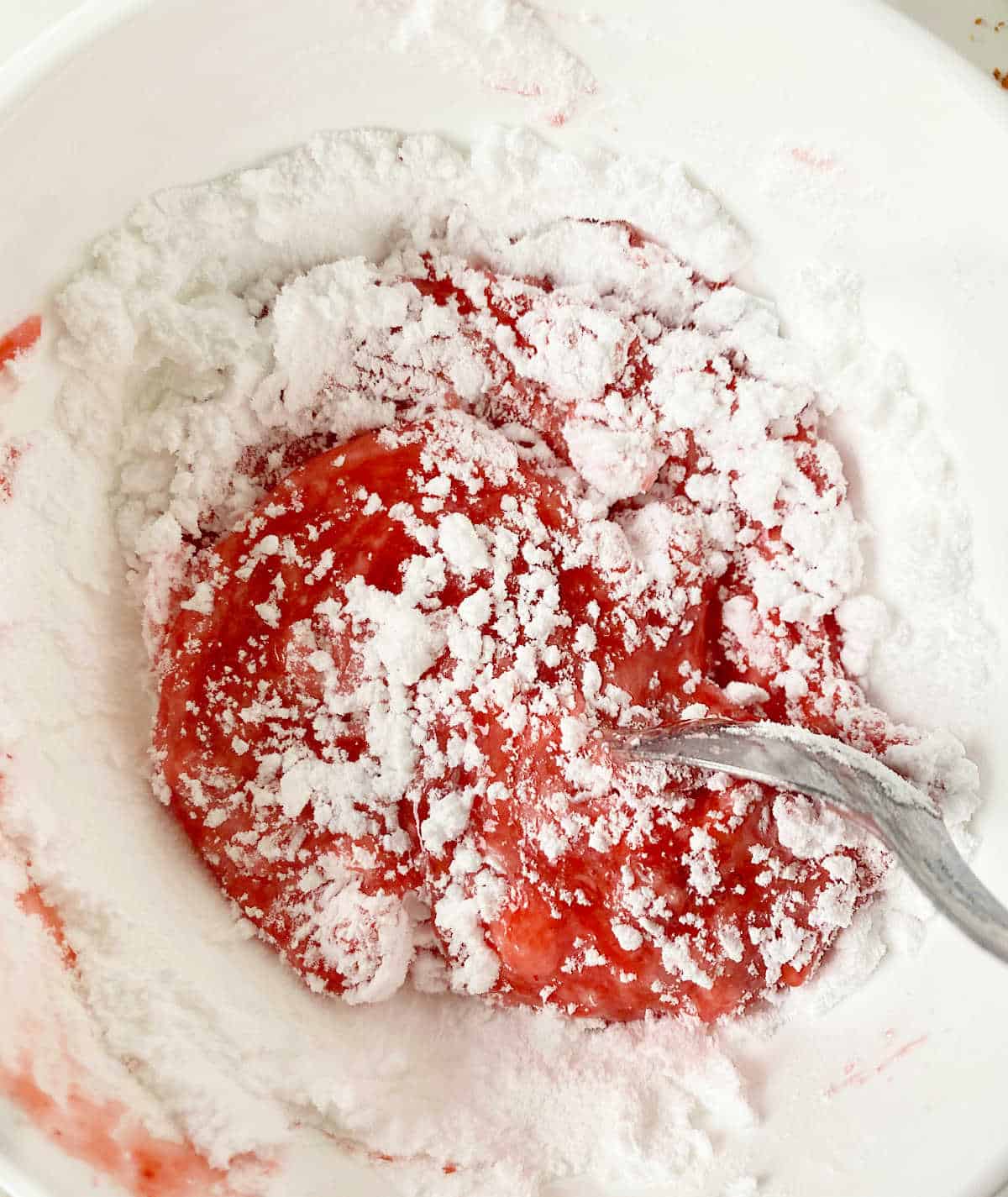White bowl with powdered sugar and strawberry puree being mixed with a spoon. 
