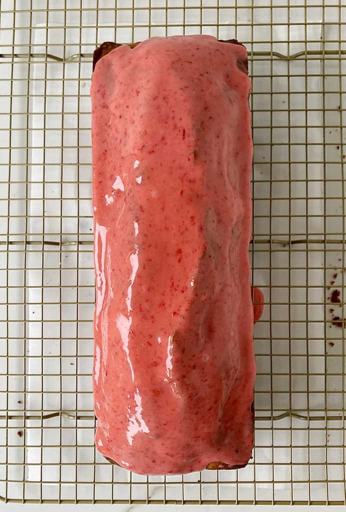 Wire rack with a loaf cake glazed with a pink icing.