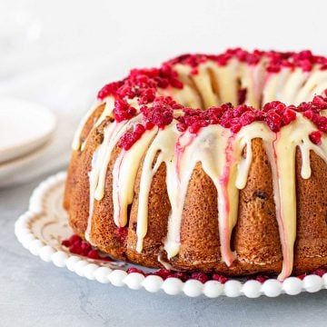 Glazed white chocolate raspberry bundt cake on a white plate, grey background.