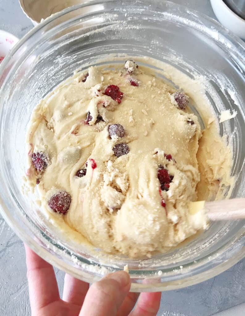 Folding raspberries and white chocolate into cake batter in a glass bowl.