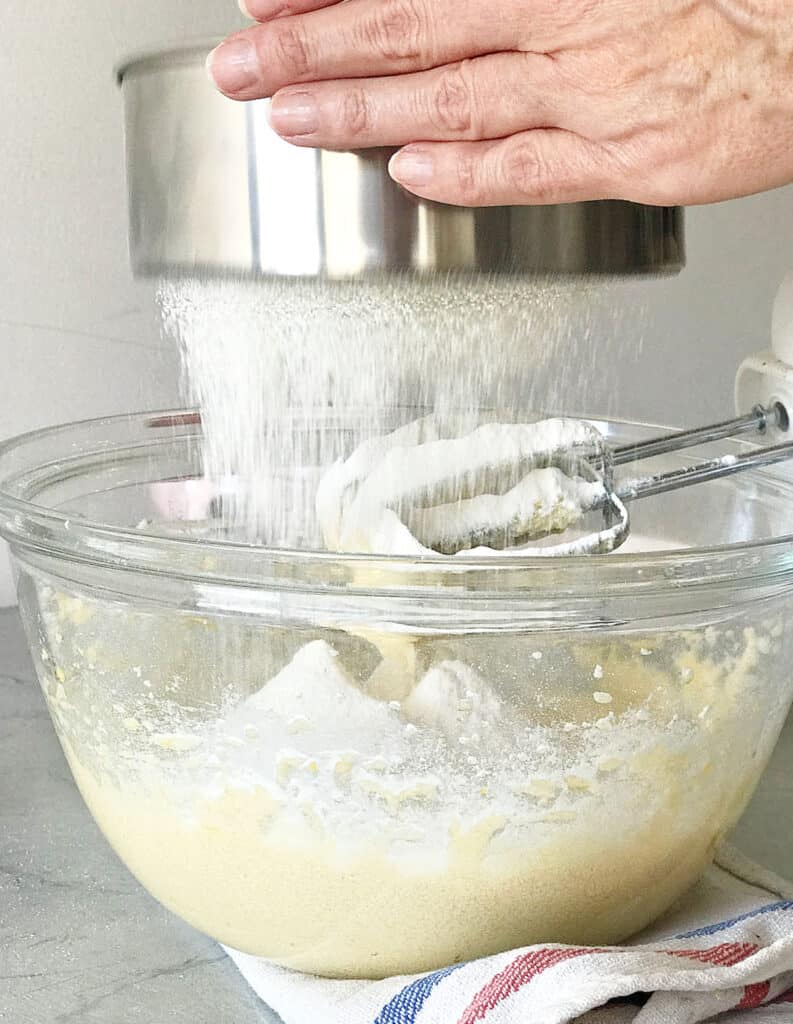 Sifting flour into a glass bowl with cake batter. Gray background. 