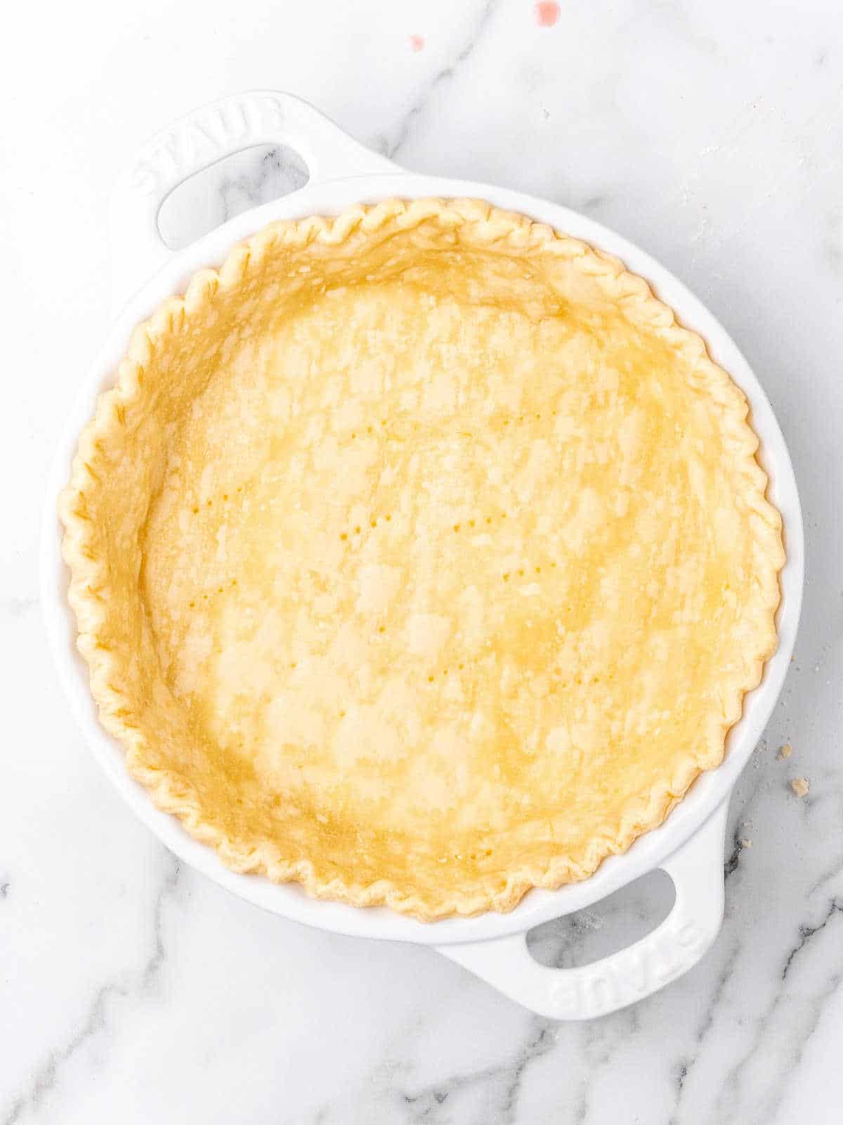 Half baked pie crust in a white pie plate on a white marbled surface.