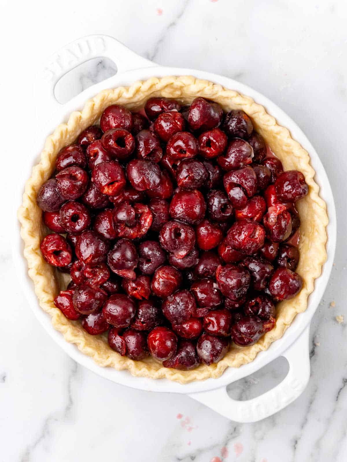 Fresh cherry pie filling in a white dish with a homemade crust. White marbled surface.