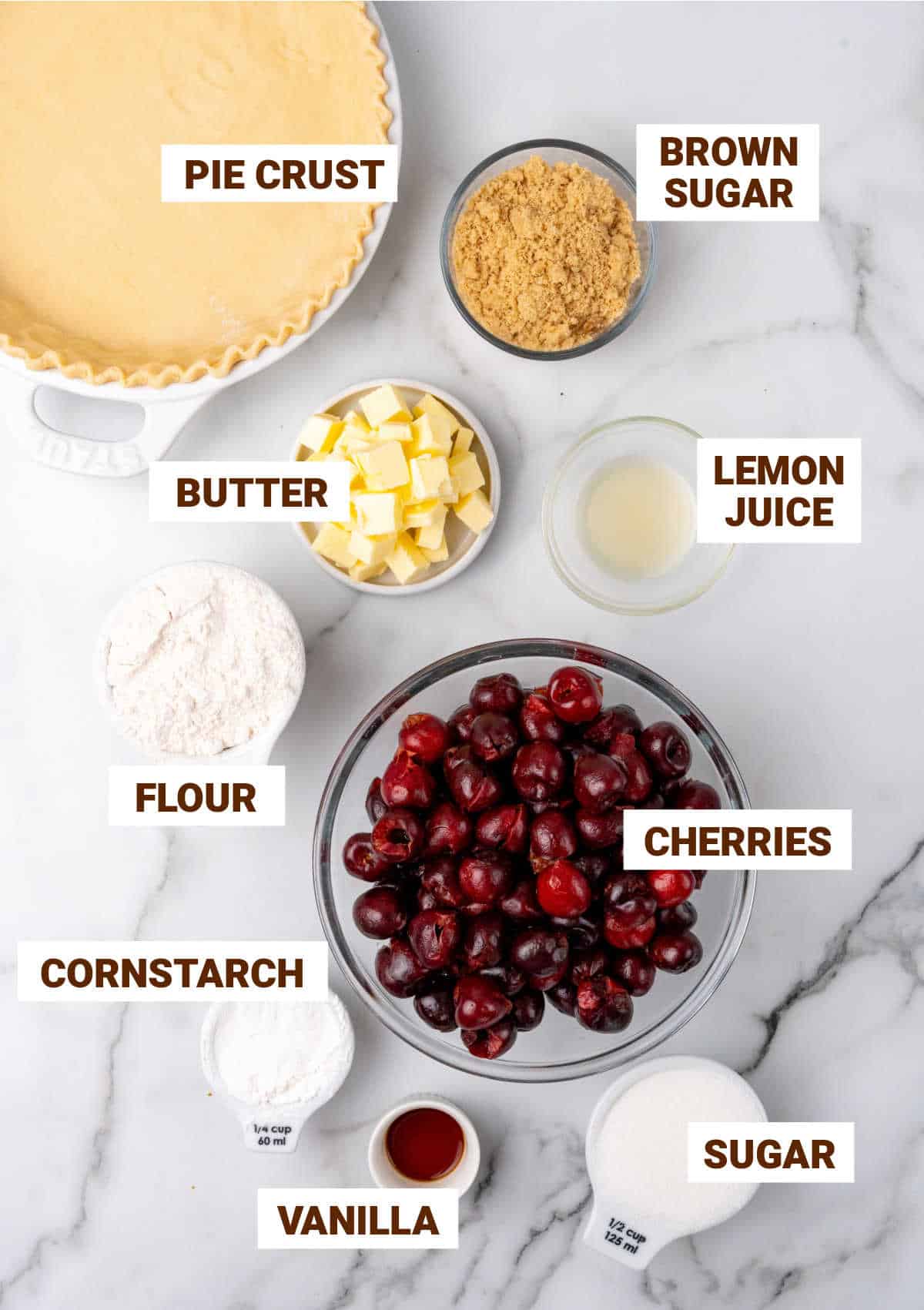 White grey marble surface with bowls containing cherry pie ingredients including pie crust, crumble, vanilla, lemon and cornstarch.