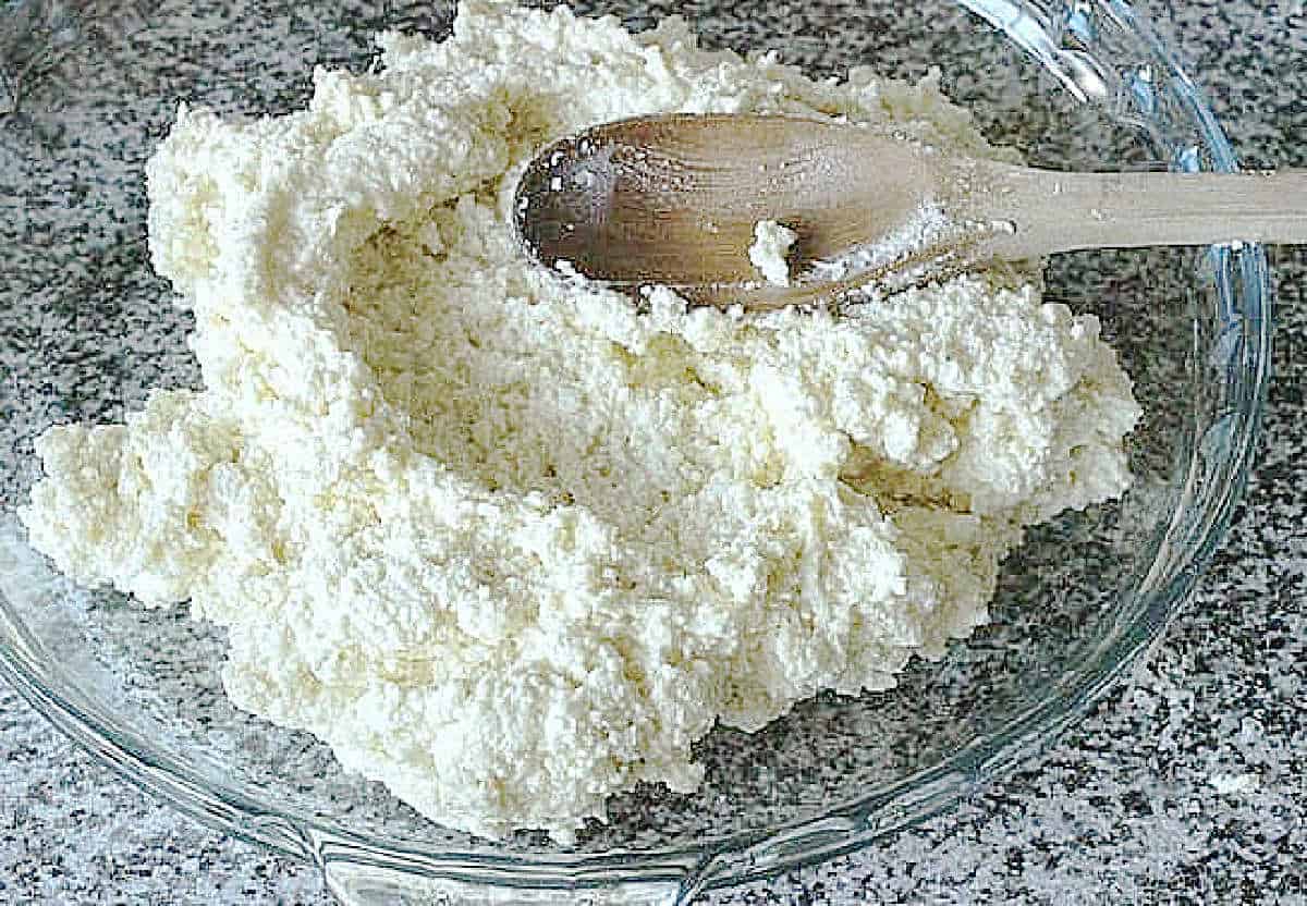 Glass plate with soft ricotta cheese and wooden spoon.