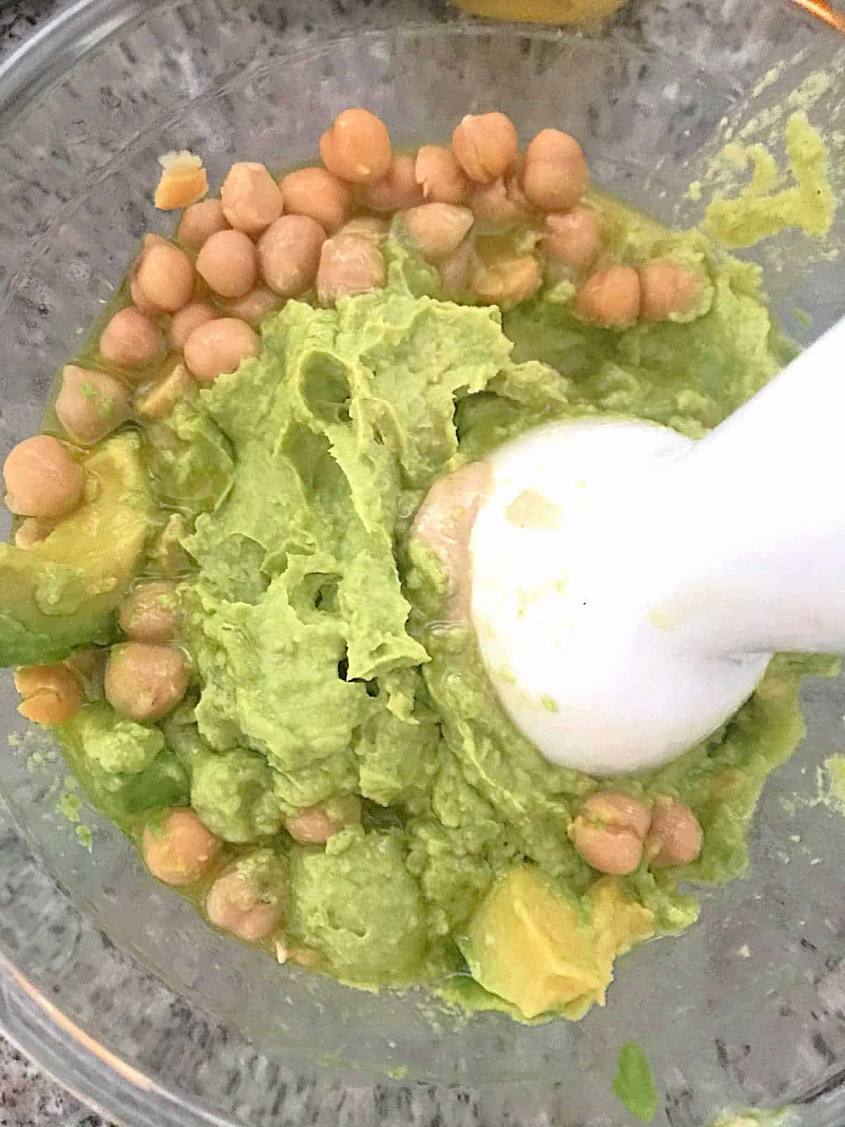 Mixing avocado with chickpeas in a glass bowl.