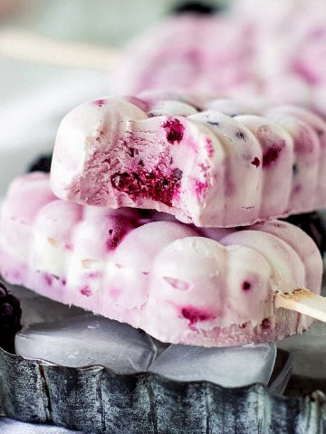 Two white and magenta ice cream paletas on a metal pan, top one is bitten.