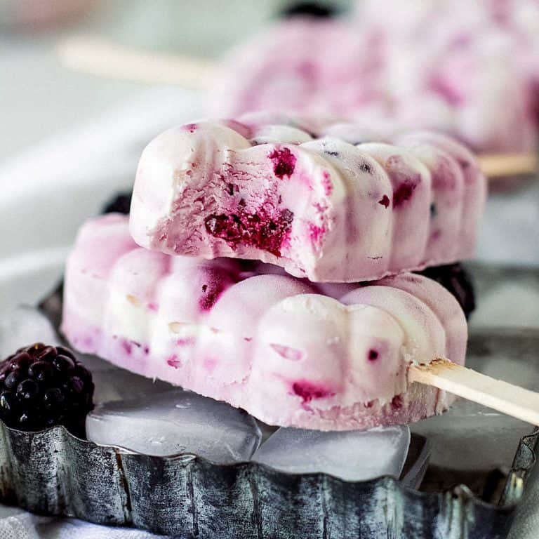 Two white and magenta ice cream paletas on a metal pan, top one is bitten.
