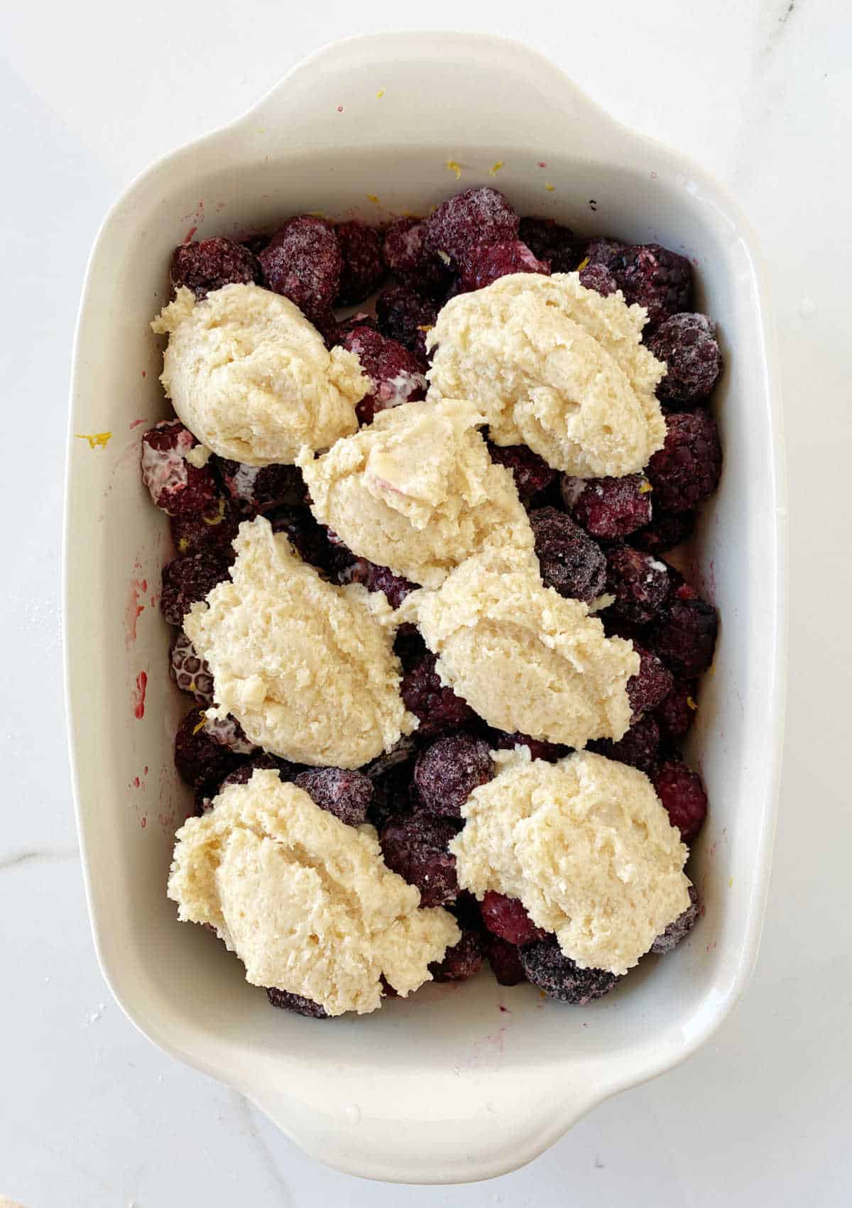 Top view of unbaked blackberry cobbler in beige ceramic dish on white surface