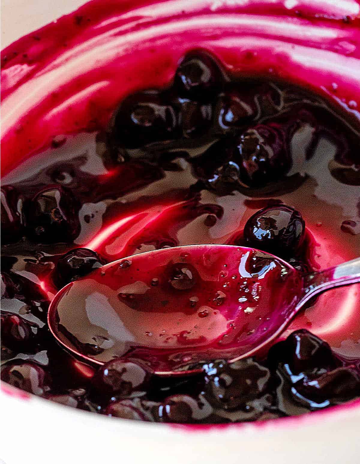 White bowl with blueberry sauce, a spoon. Very close up image. 