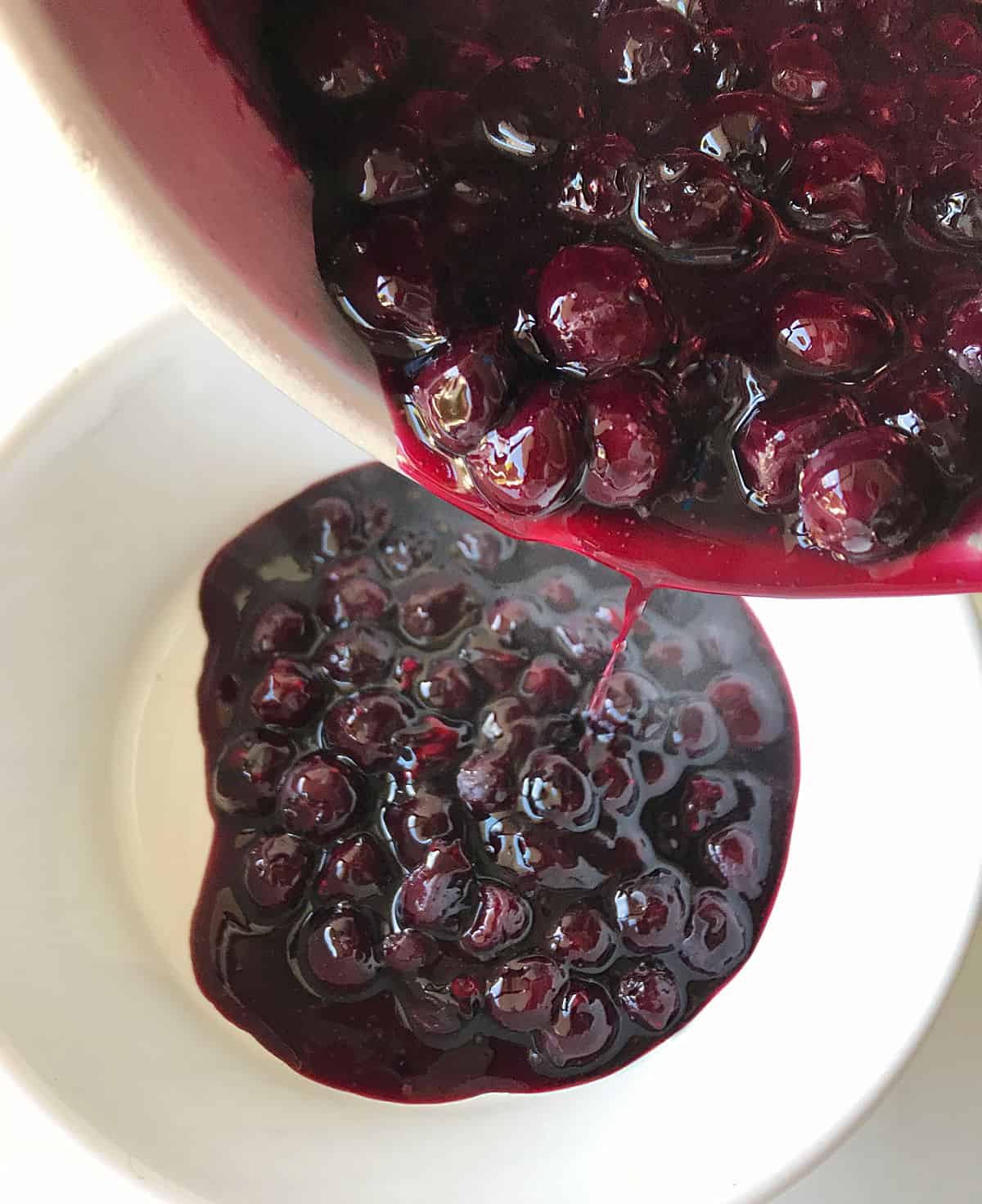 Transferring blueberry sauce from saucepan to white bowl