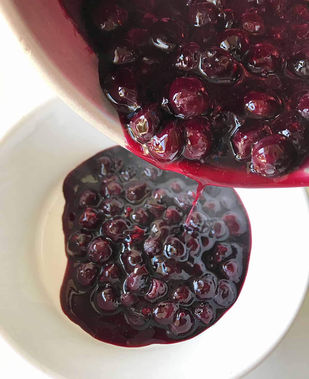 Transferring blueberry sauce from saucepan to white bowl.