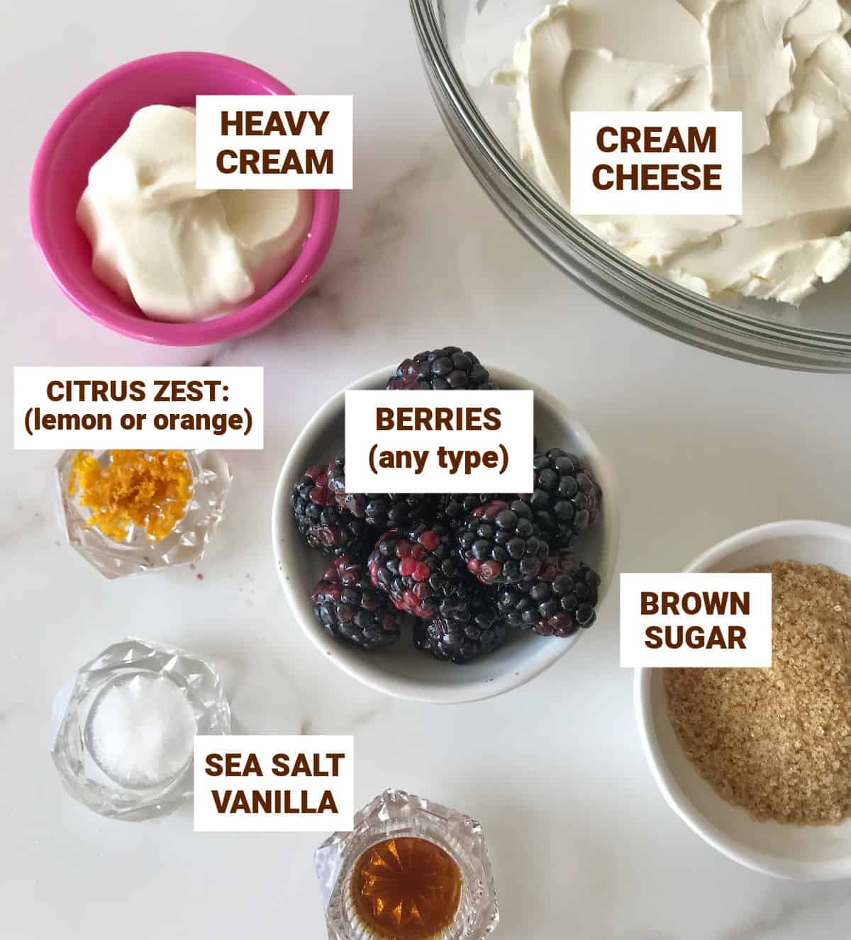 Ingredients for cheesecake berry ice cream in bowls on white surface including berries, cream, brown sugar, zest.