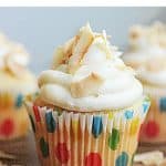 Cream cheese frosted cupcakes in dotted paper liners, wooden table, bluish background