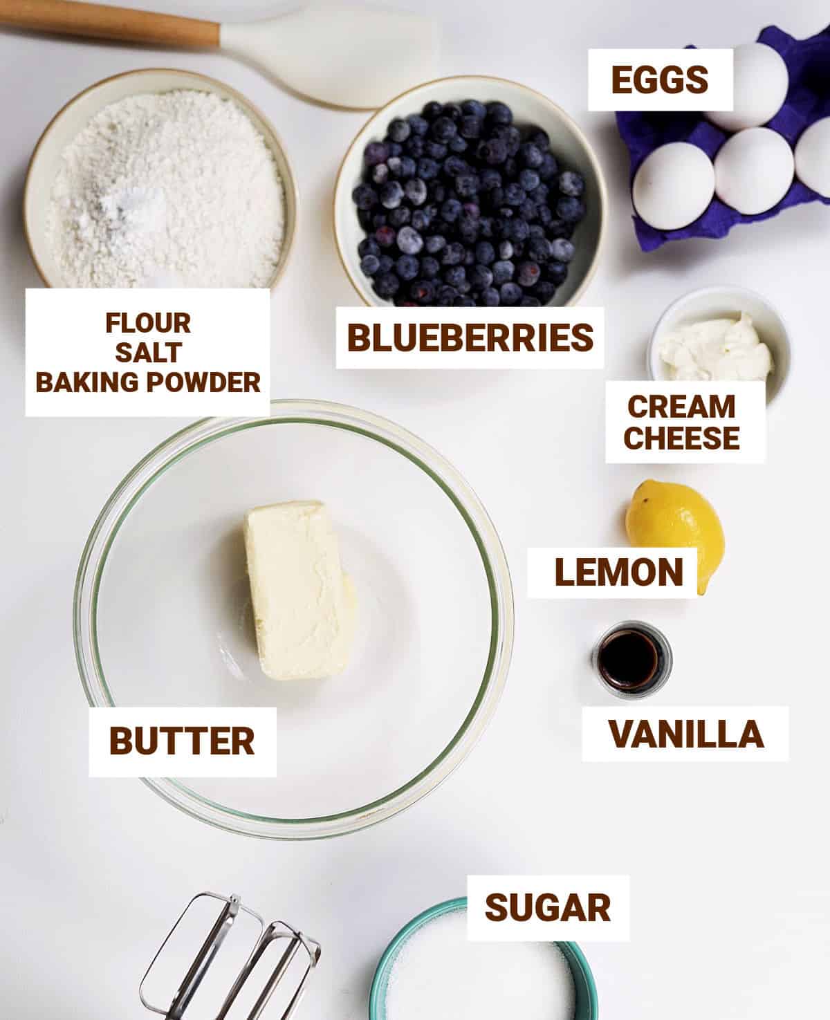 White surface with bowls containing lemon blueberry cake ingredients including butter, vanilla, flour mixture, sugar.