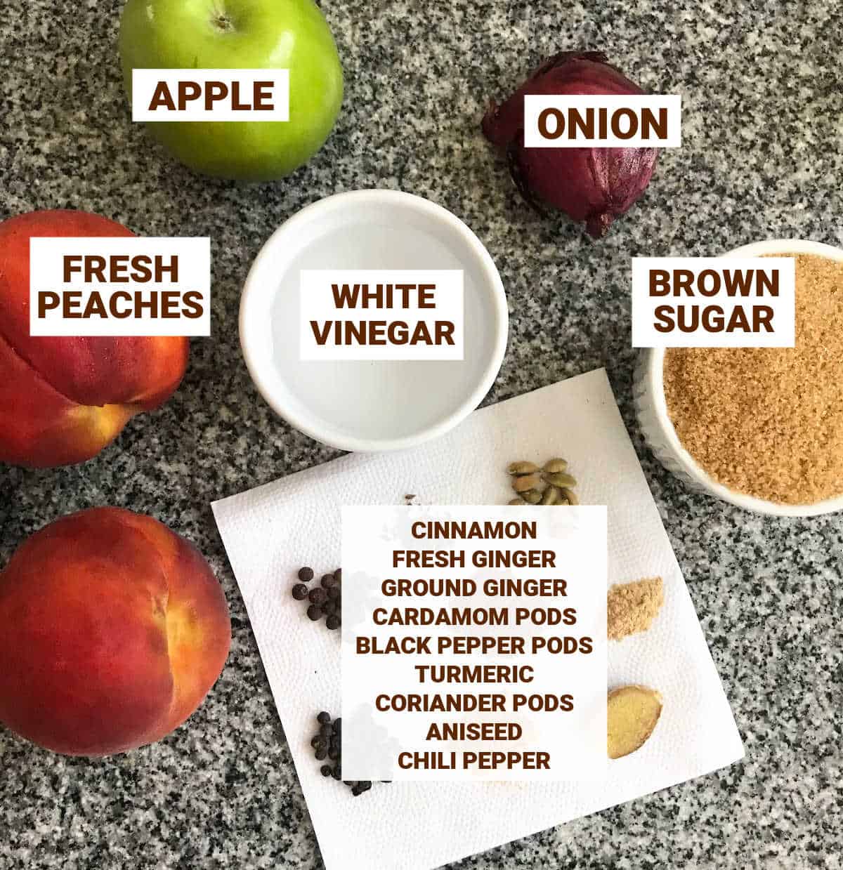Ingredients for peach chutney on grey marble surface including spices, apple, onion, vinegar, and sugar.