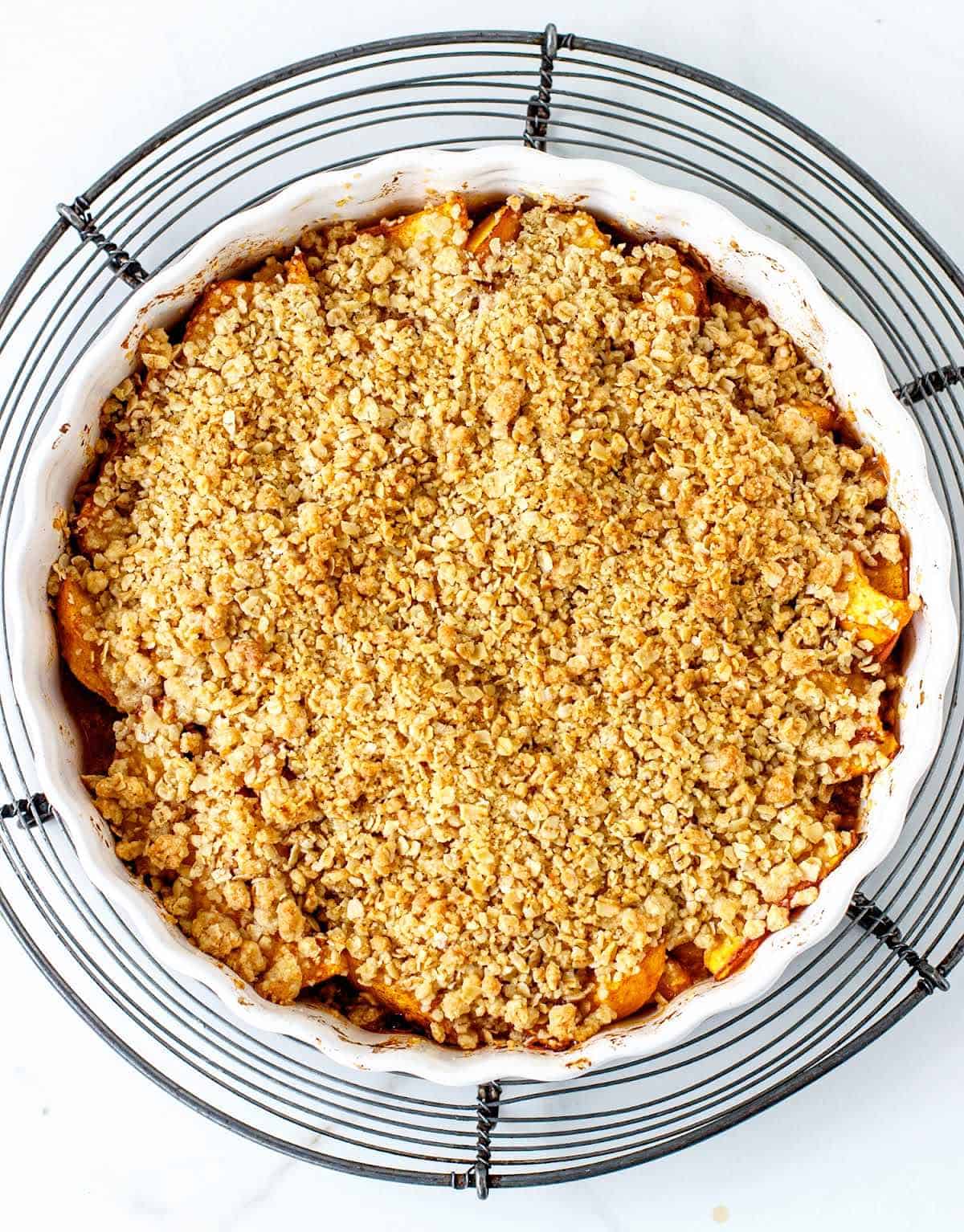 Baked peach crisp on wire rack on white surface.