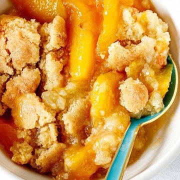 Close view of peach dump cake serving in white bowl with a teal spoon.