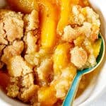Top view of peach dump cake serving in white bowl, a green blueish spoon in it