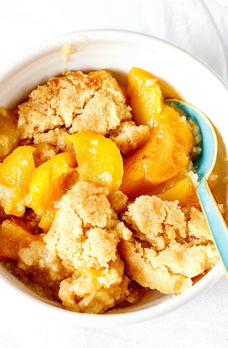 A white bowl with peach dump cake, blue spoon