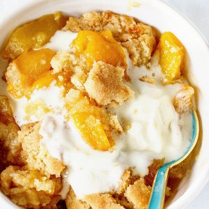 Serving of peach dump cake with ice cream in a white bowl with a teal spoon.