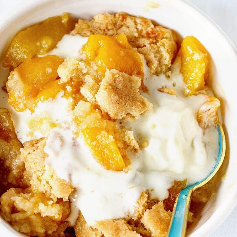 Serving of peach dump cake with ice cream in a white bowl with a teal spoon.