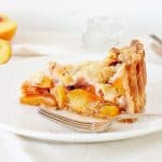 Slice of peach pie on a white plate with silver fork, a white background.