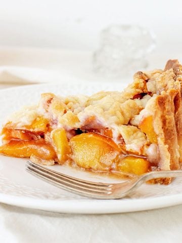 Slice of peach pie on a white plate with silver fork, a white background.