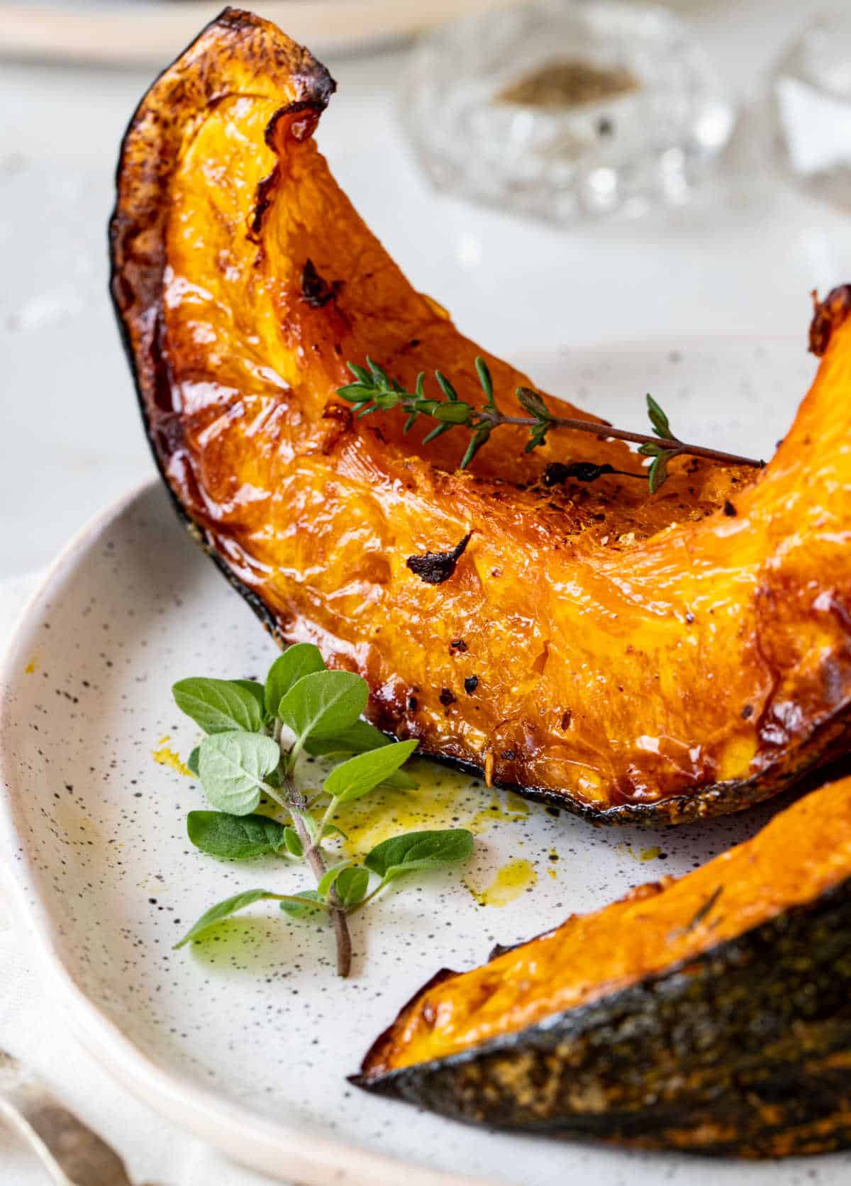 Close up of partial roasted pumpkin wedges on white plate, fresh herbs.