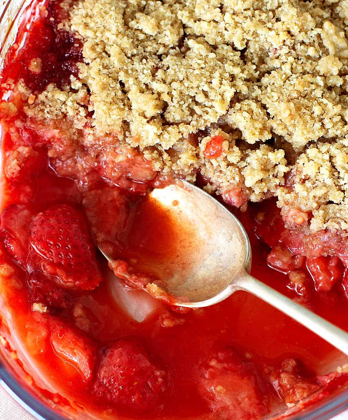 Silver spoon in pool of strawberry crisp on glass dish