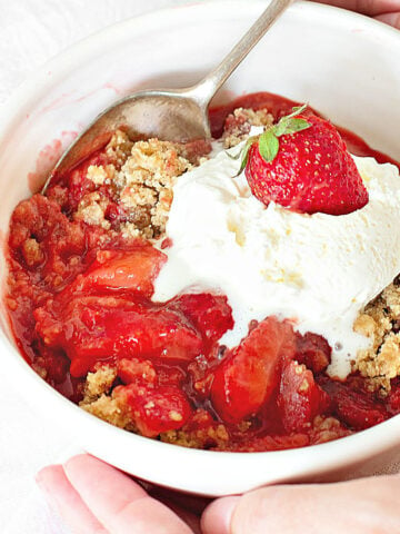 White bowl with serving of strawberry crisp with ice cream scoop. Silver spoon.