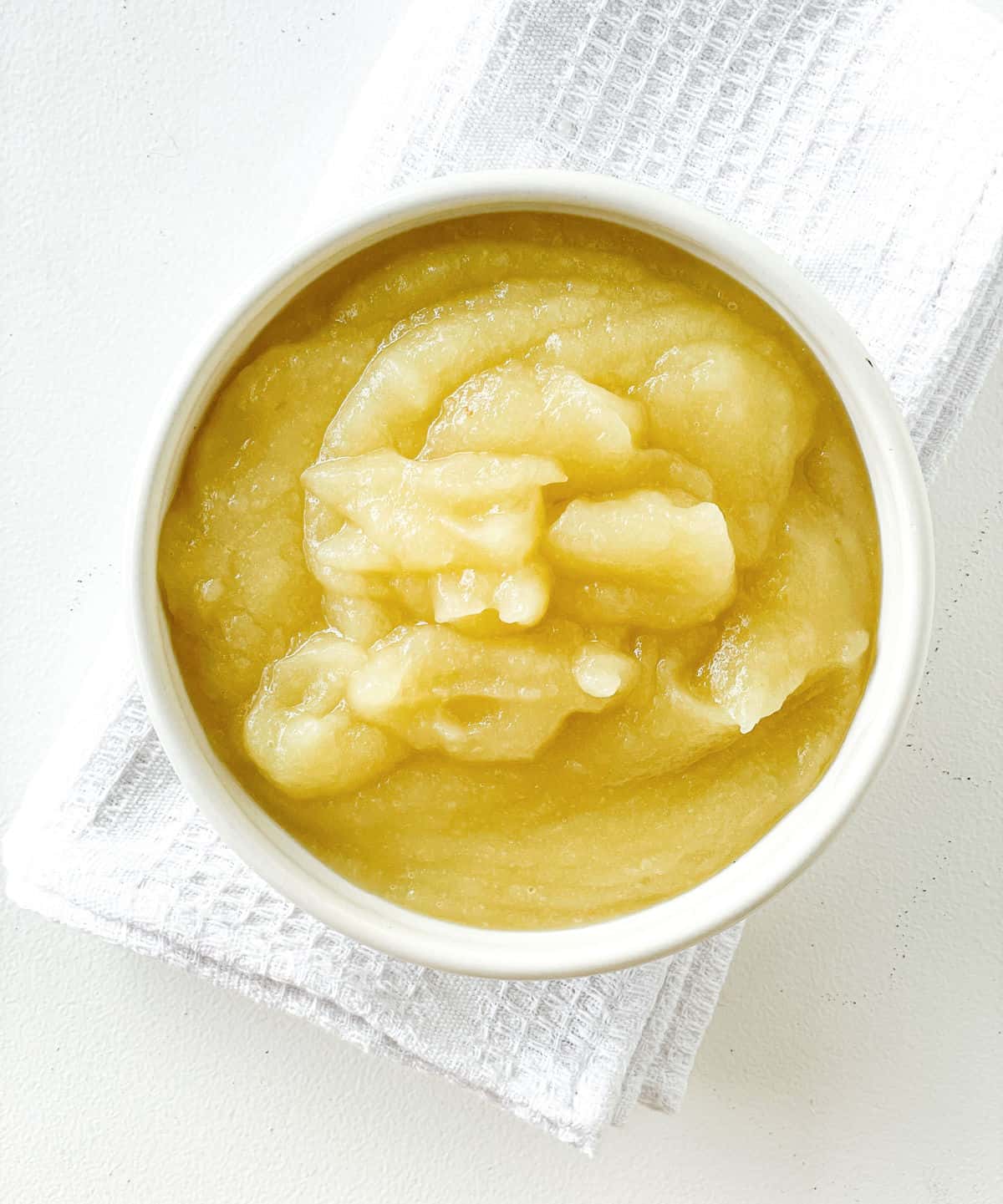 White bowl with applesauce on white cloth and surface.