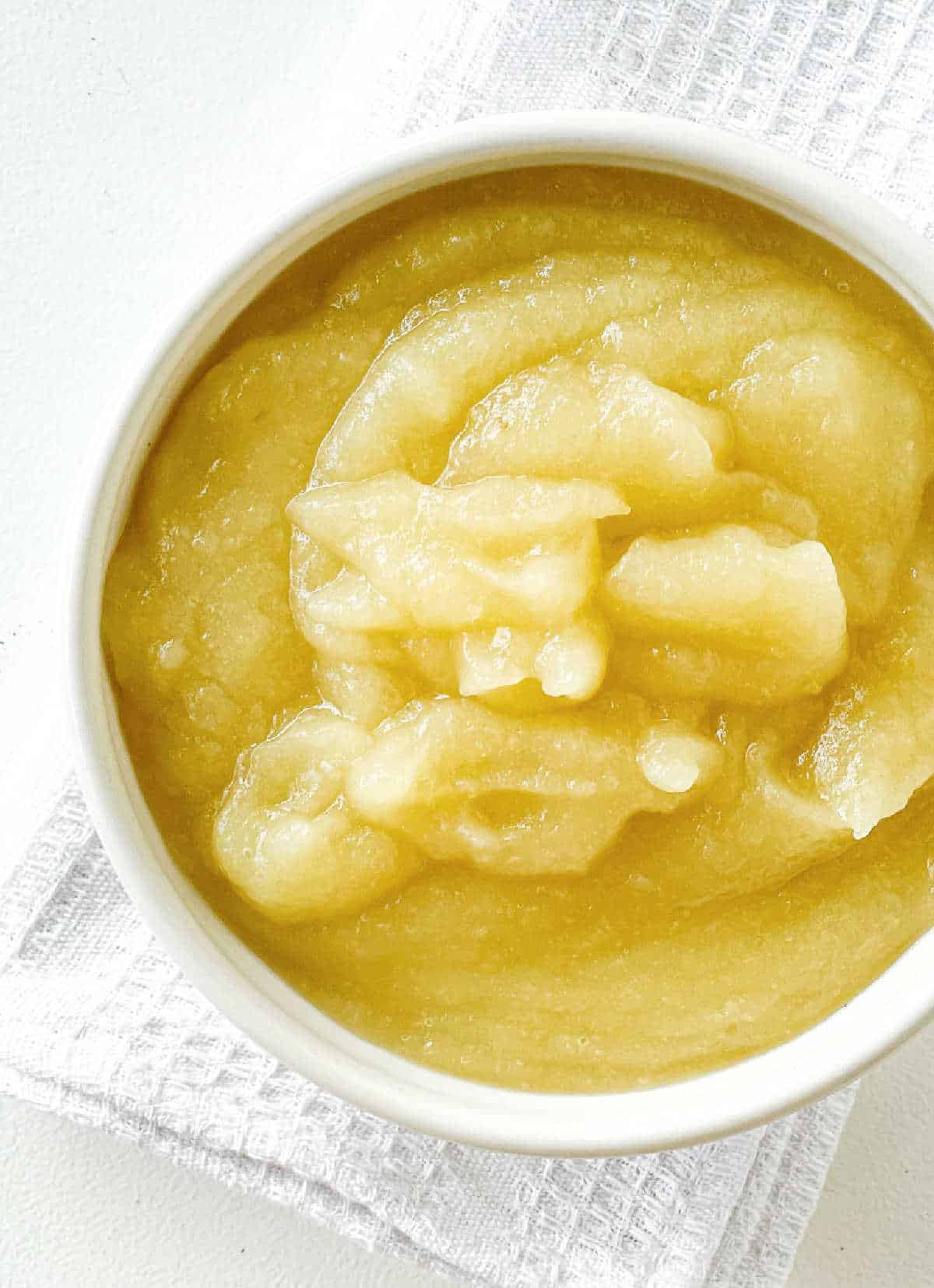 Partial view of white bowl with applesauce on a white kitchen towel and surface