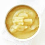 Top view of a white bowl with applesauce on white cloth and surface.