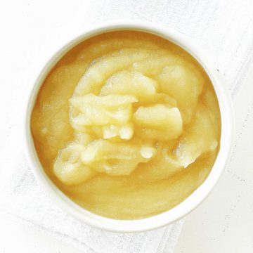 Top view of a white bowl with applesauce on white cloth and surface.