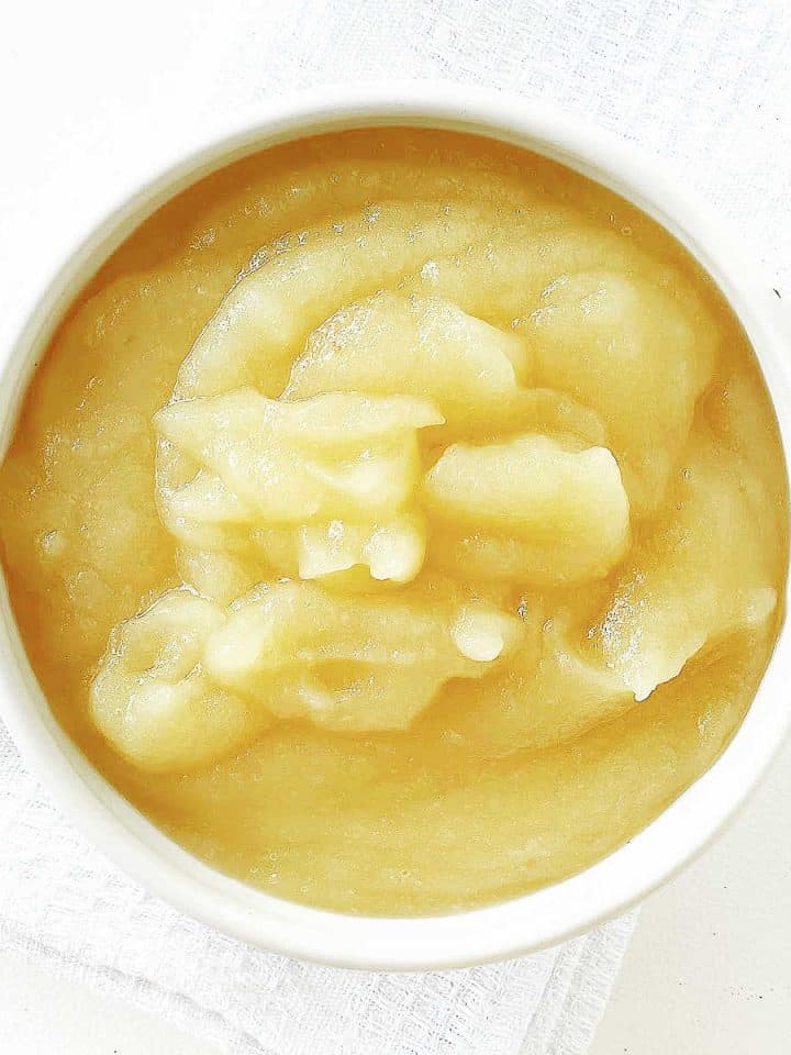 Top view of a white bowl with applesauce on white cloth and surface.
