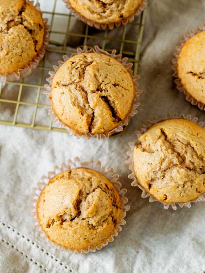 Several applesauce muffins on a beige cloth and golden colored wire rack.