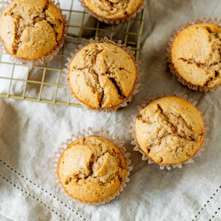 Several applesauce muffins on a beige cloth and golden colored wire rack.