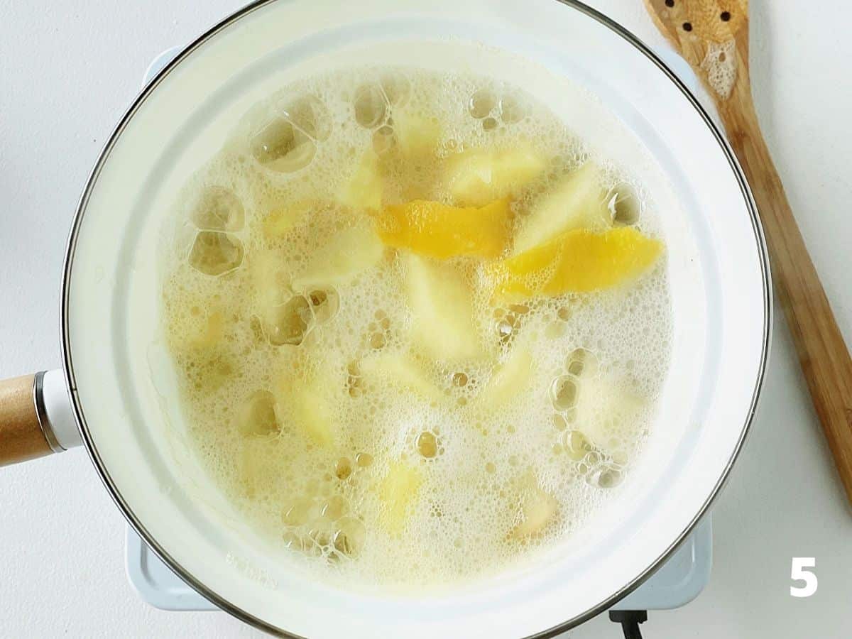 Top view of white saucepan with apples and lemon peel simmering, white surface