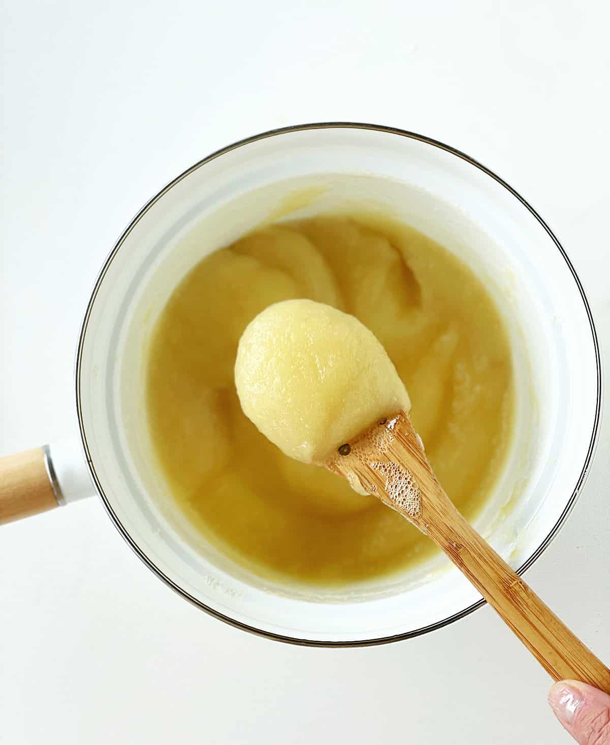 Spooning applesauce from a white saucepan beneath, white surface