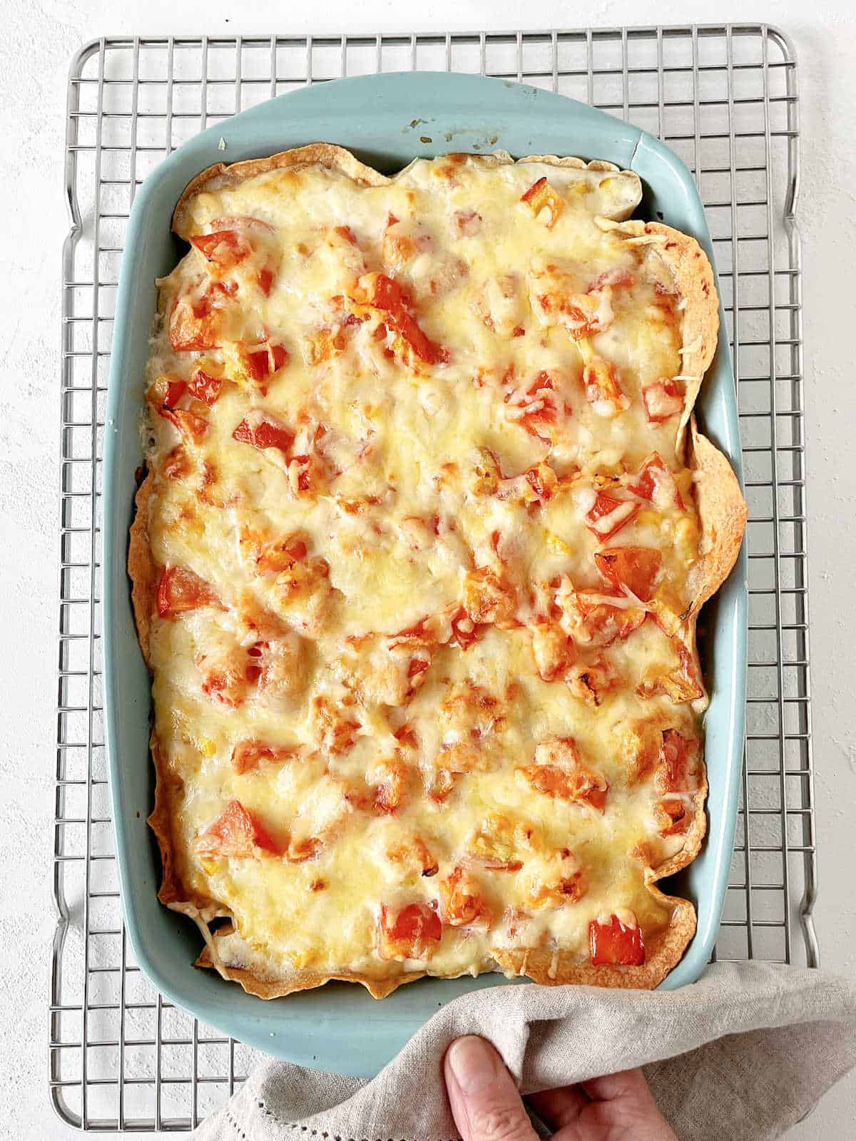 Baked cheese and tomato topped casserole in blue dish on wire rack.