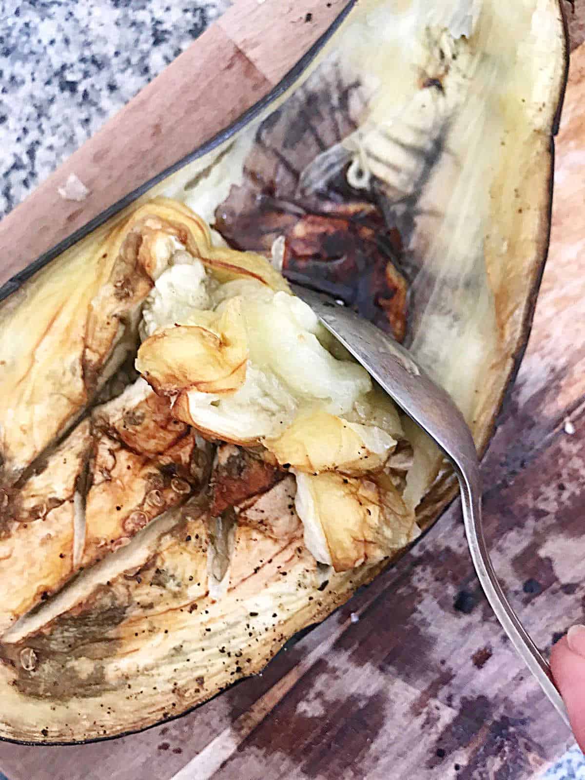 Scooping pulp from baked eggplant half with a spoon