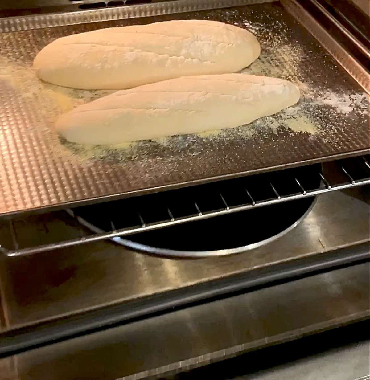Metal pan with loaves of bread in the oven, a pan with water in the bottom 