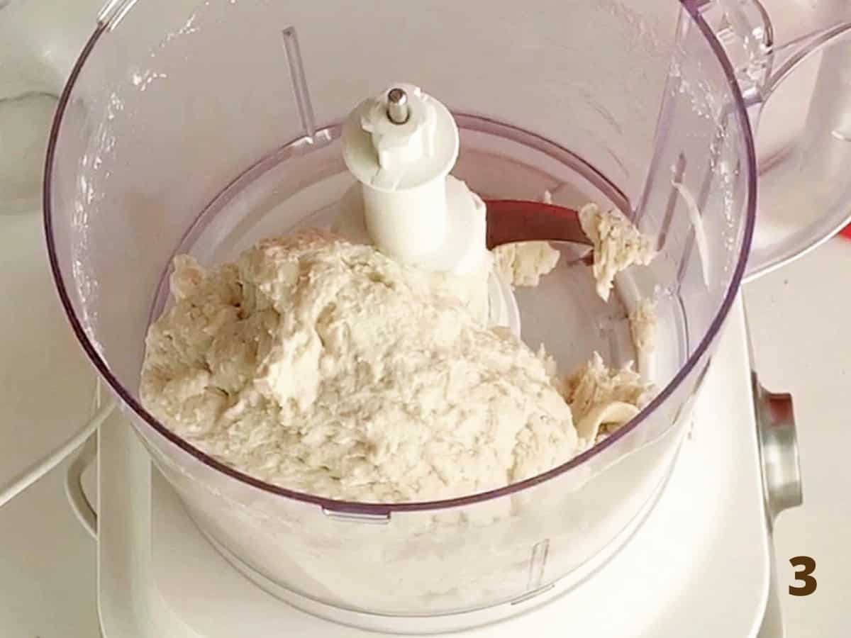 Bowl of food processor with bread dough inside, white background