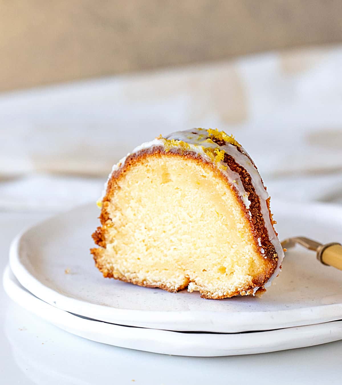 Single slice of lemon bundt cake on stack of white plates