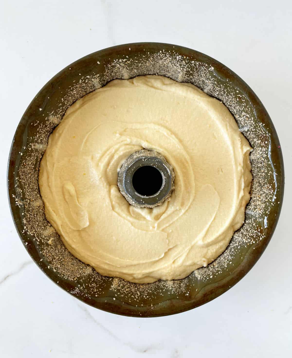 Bundt cake batter in dark metal pan on a white surface